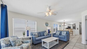A living room with a blue sofa set, a coffee table, and a ceiling fan. - Dreamy island escape with beach access, pool & complimentary seasonal beach service (Fort Walton Beach)