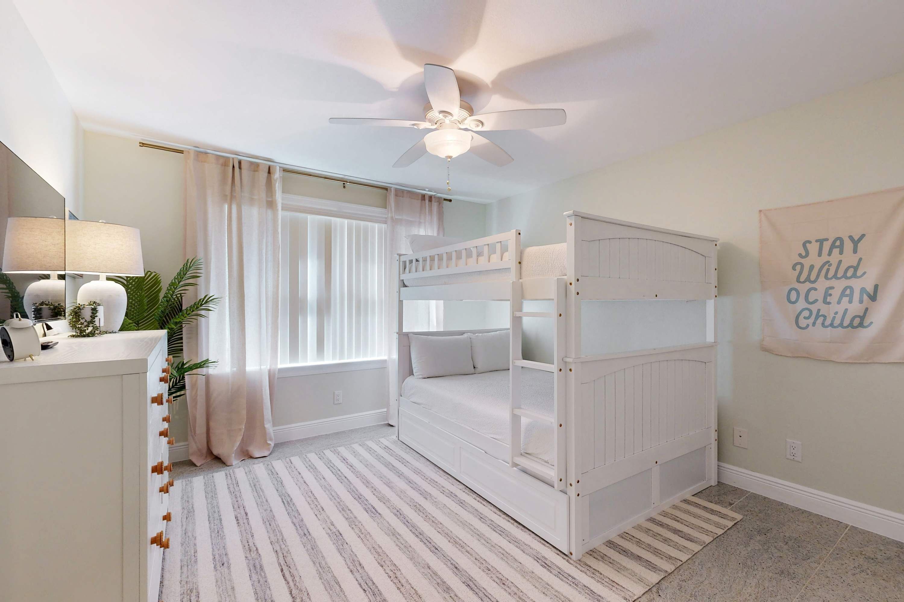 Habitación apta para niños con literas, ventilador de techo y un cartel motivacional.