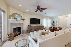A living room with a fireplace, a large flat-screen TV, a ceiling fan, and a sofa.