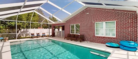 A swimming pool with a glass ceiling, surrounded by a red brick building with a window and a door.