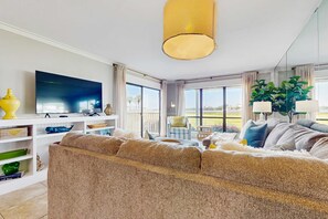 Ein modernes Wohnzimmer mit einem großen Flachbildfernseher, einem beigen Sofa und einem Essbereich mit Tisch und Stühlen.