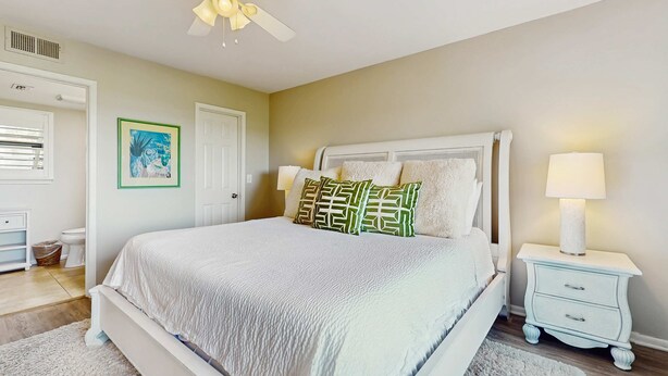 A bedroom with a bed, nightstand, lamp, ceiling fan, and a framed picture on the wall. - Townhome with bay & golf views, golf cart, pool, & beach tram (Miramar Beach)