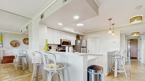 A modern kitchen with white cabinetry, stainless steel appliances, and a central island with bar stools. - Townhome with bay & golf views, golf cart, pool, & beach tram (Miramar Beach)