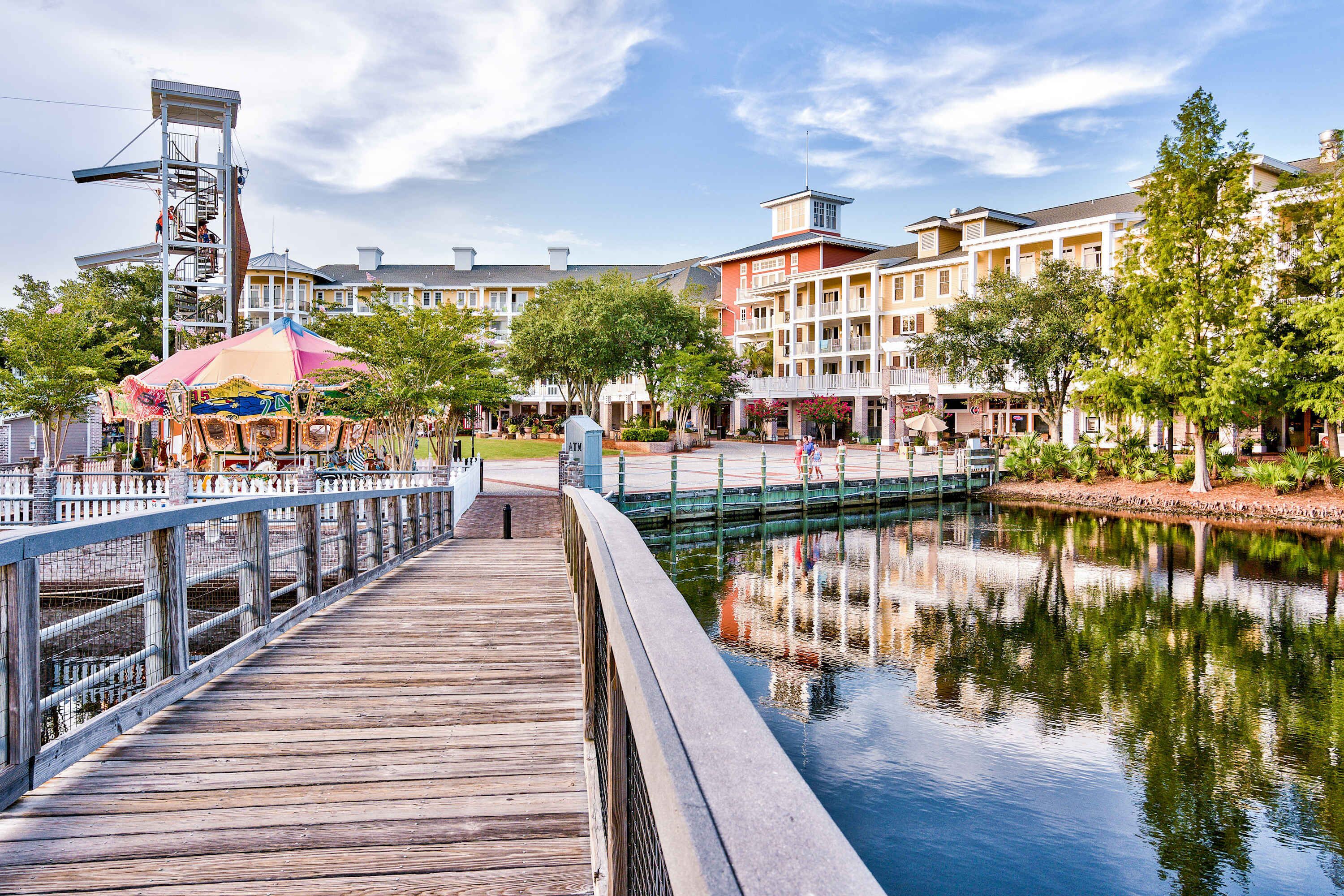 A wooden boardwalk leading to a waterfront area with a carousel and buildings in the background.