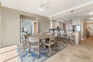 Une cuisine spacieuse avec un coin repas, comprenant un grand îlot central, des meubles blancs et un ventilateur de plafond.