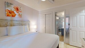 Une chambre d’hôtel avec un grand lit, des murs blancs, un ventilateur de plafond et une porte donnant sur une autre pièce.