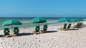 Une plage bordée de rangées de chaises de plage et de parasols verts, disposés sur le sable.