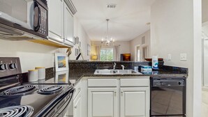 Une cuisine moderne avec des meubles blancs, une cuisinière noire, un lave-vaisselle et un plan de travail en granit.