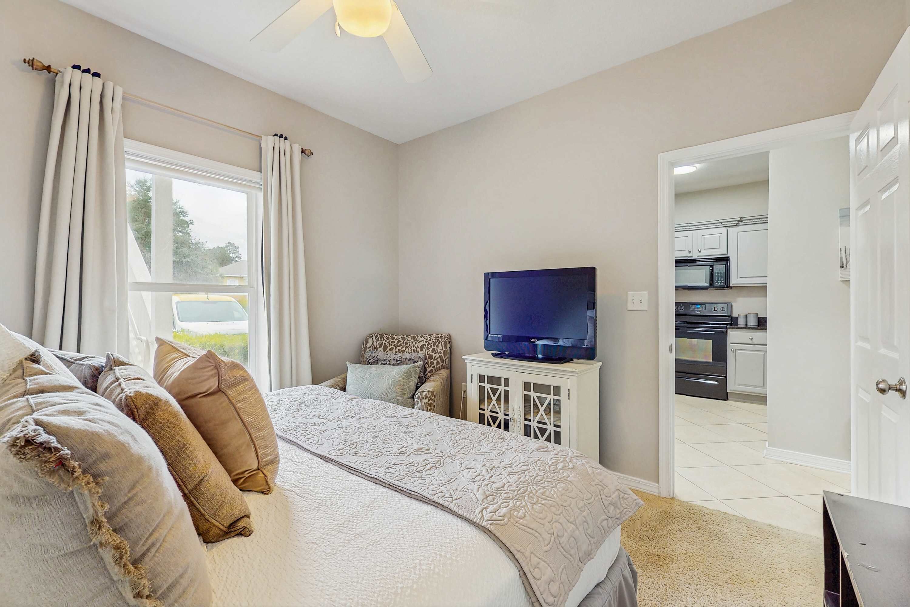 A bedroom with a bed, pillows, a television, and a view of the kitchen.