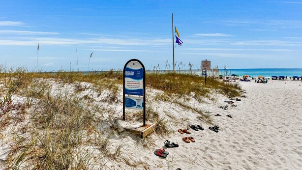 Une plage avec un panneau indicateur, un drapeau de plage et un mât.