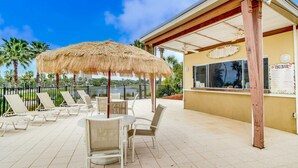 A covered outdoor seating area with a thatched umbrella, lounge chairs, and a tiki bar sign. - Luxurious condo near downtown, beach, & golf with pools & tennis (Miramar Beach)