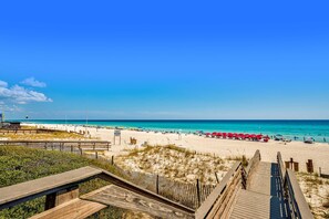 Een strand met een houten pier die naar de kust loopt, een helderblauwe lucht en turquoise water.