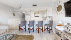 A modern kitchen with a central island, bar stools, and a large wall clock. - Large waterfront cottage, Private pool, Close to entertainment (Miramar Beach)