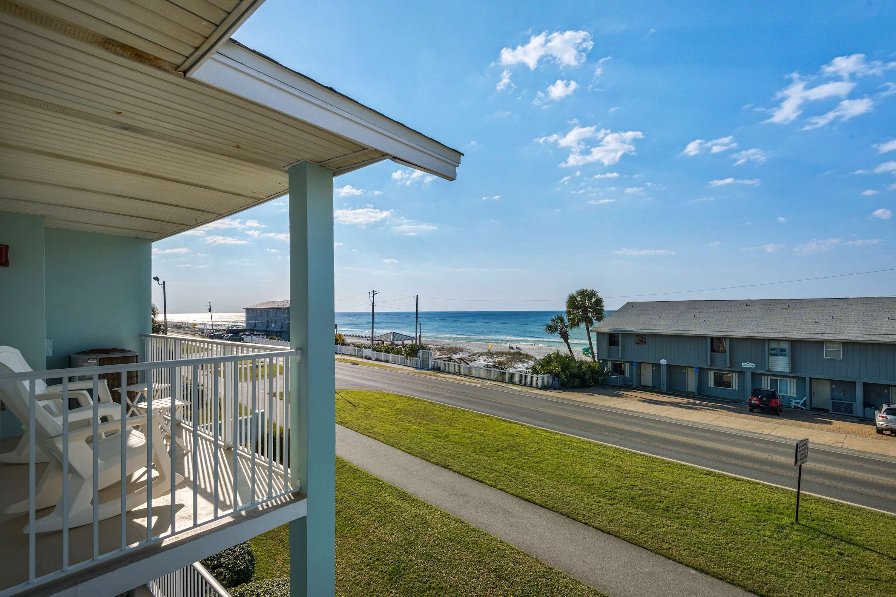 A balcony with outdoor seating, a view of the beach, and a road with cars.