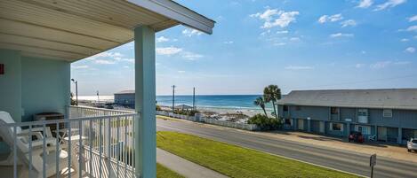 A balcony with outdoor seating, a view of the beach, and a road with cars.