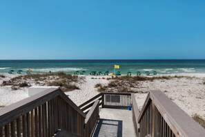 Une promenade en bois menant à une plage de sable, agrémentée de parasols et de chaises de plage.