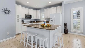 A kitchen with white cabinets, a granite countertop, a microwave, a refrigerator, and a clock on the wall. - Destin Mojo (Miramar Beach)