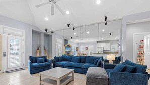 A modern living room with a sectional sofa, a coffee table, and a mirrored wall reflecting the kitchen area. - Destin Mojo (Miramar Beach)