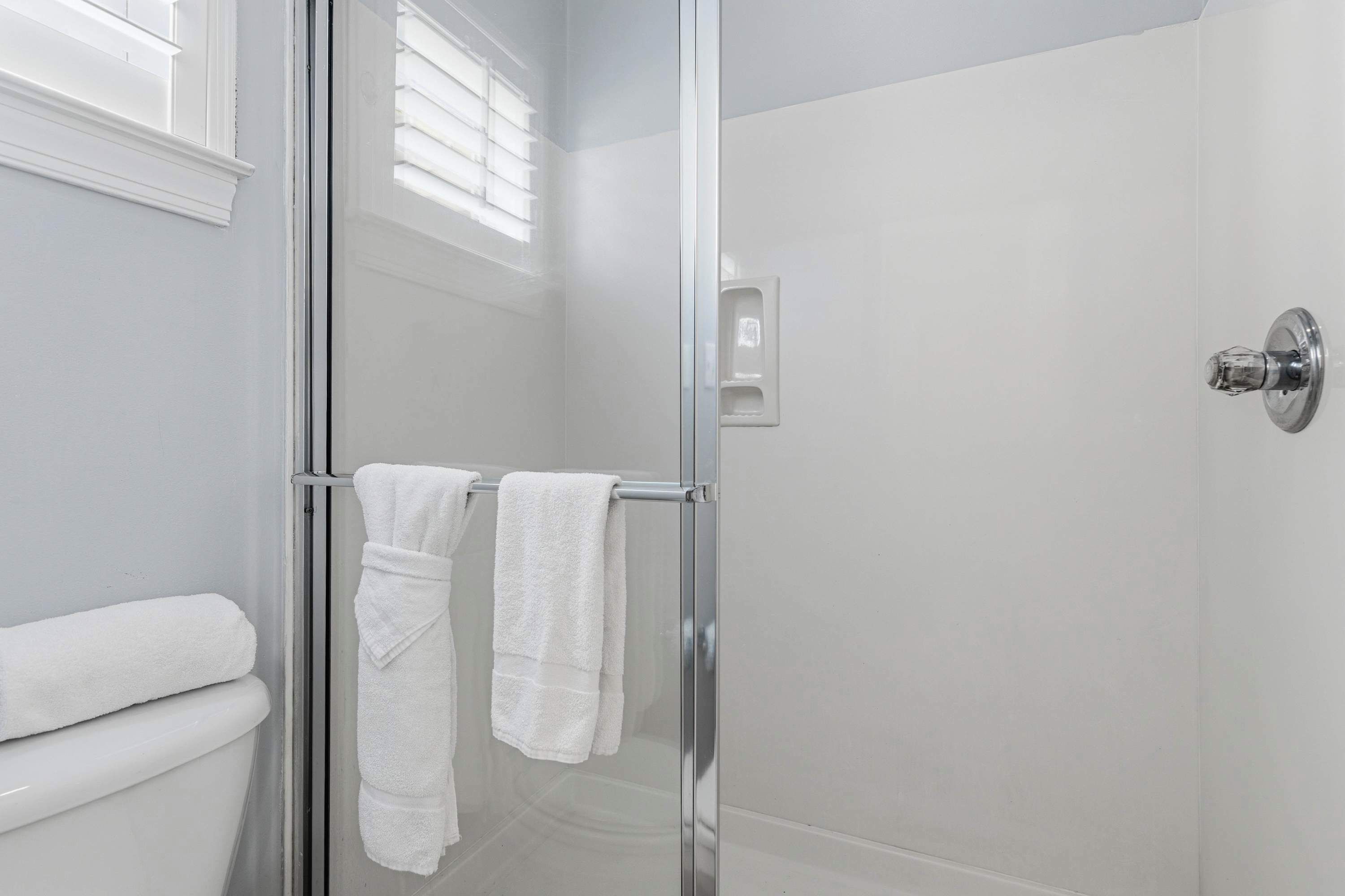 Un bany modern amb una cabina de dutxa de vidre, un vàter i un suport de tovalloles amb dues tovalloles.