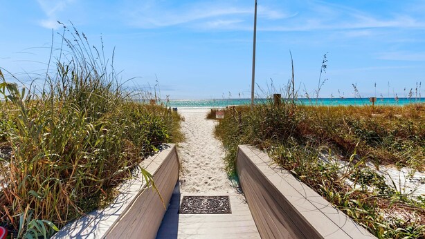 Ein sandiger Weg führt zu einem Strand, auf dem eine Fahne weht.