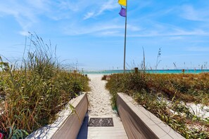 A sandy pathway leading to a beach with a flag on a pole. - Cozy coastal condo with kitchen, shared pool and beach access (Miramar Beach)
