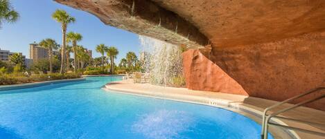 Una piscina con cascada, rodeada de palmeras y una estructura de roca roja.