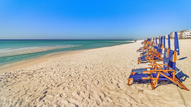 A beach with rows of blue and orange beach chairs and umbrellas, a sandy shore, and a clear blue sky. - Luau getaway with pools, hot tub, beach access, & private balcony (Miramar Beach)