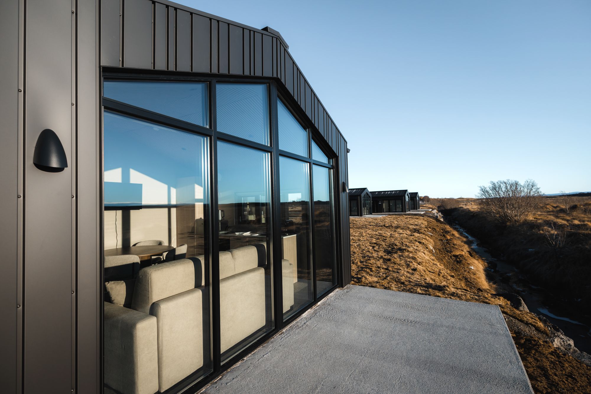 Un edificio moderno con amplios ventanales de vidrio, una terraza de concreto y vista a un paisaje árido.