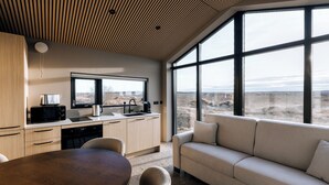 A modern kitchen with a dining area, large windows, and a view of the landscape. - Green Geysir Cottage (Bláskógabyggð)