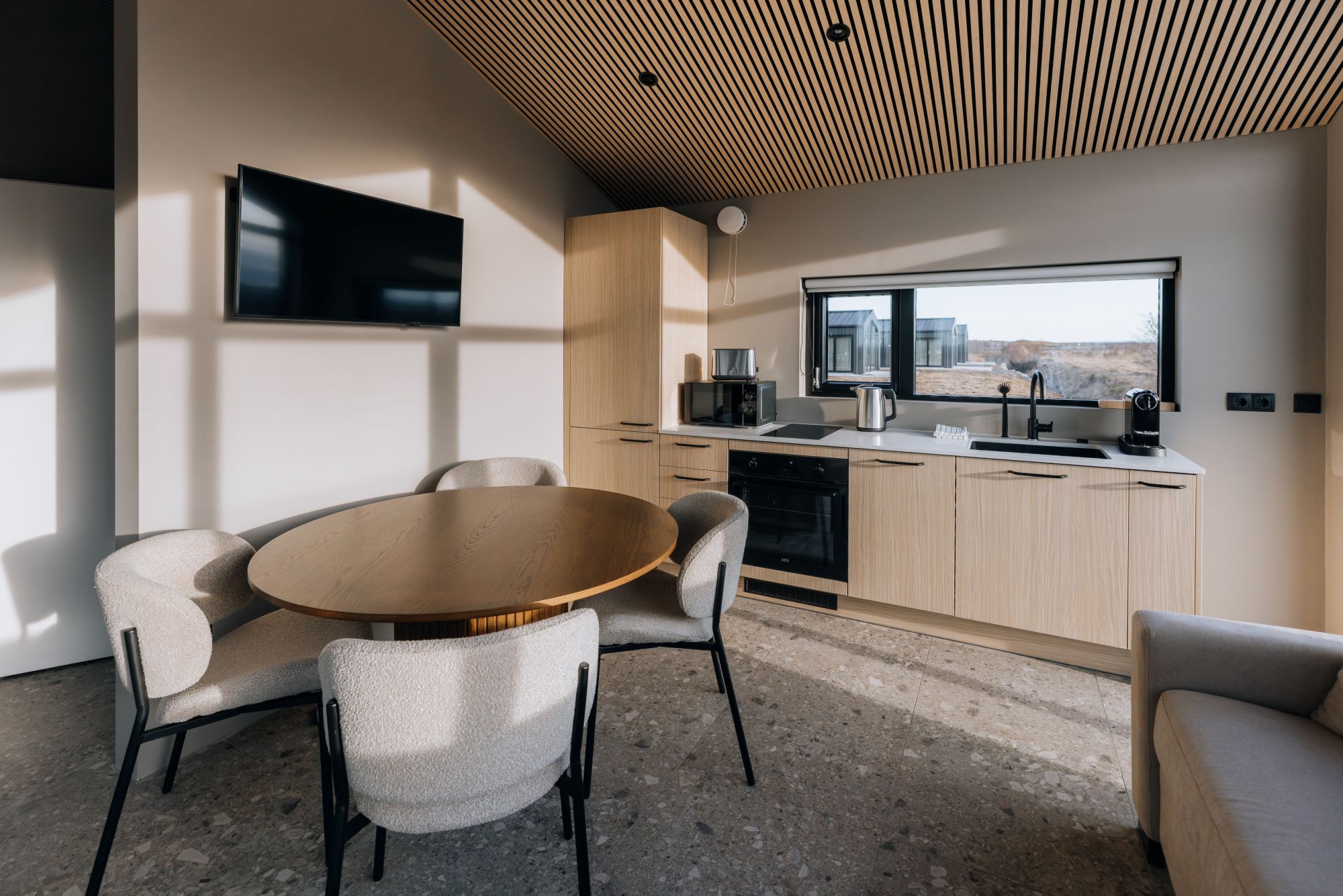 A modern kitchen with a large window, a flat-screen TV, and a dining area with a round table and chairs.