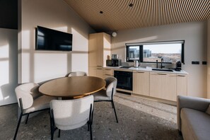 A modern kitchen with a large window, a flat-screen TV, and a dining area with a round table and chairs. - Green Geysir Cottage (Bláskógabyggð)