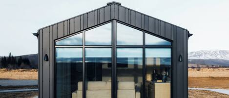 A modern, minimalist building with large glass windows and a concrete base, set in a natural landscape with mountains in the background.