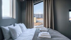 A modern hotel room with a large bed, a view of the outdoors, and a skylight. - Green Geysir Cottage (Bláskógabyggð)