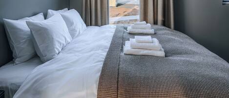 A modern hotel room with a large bed, a view of the outdoors, and a skylight.