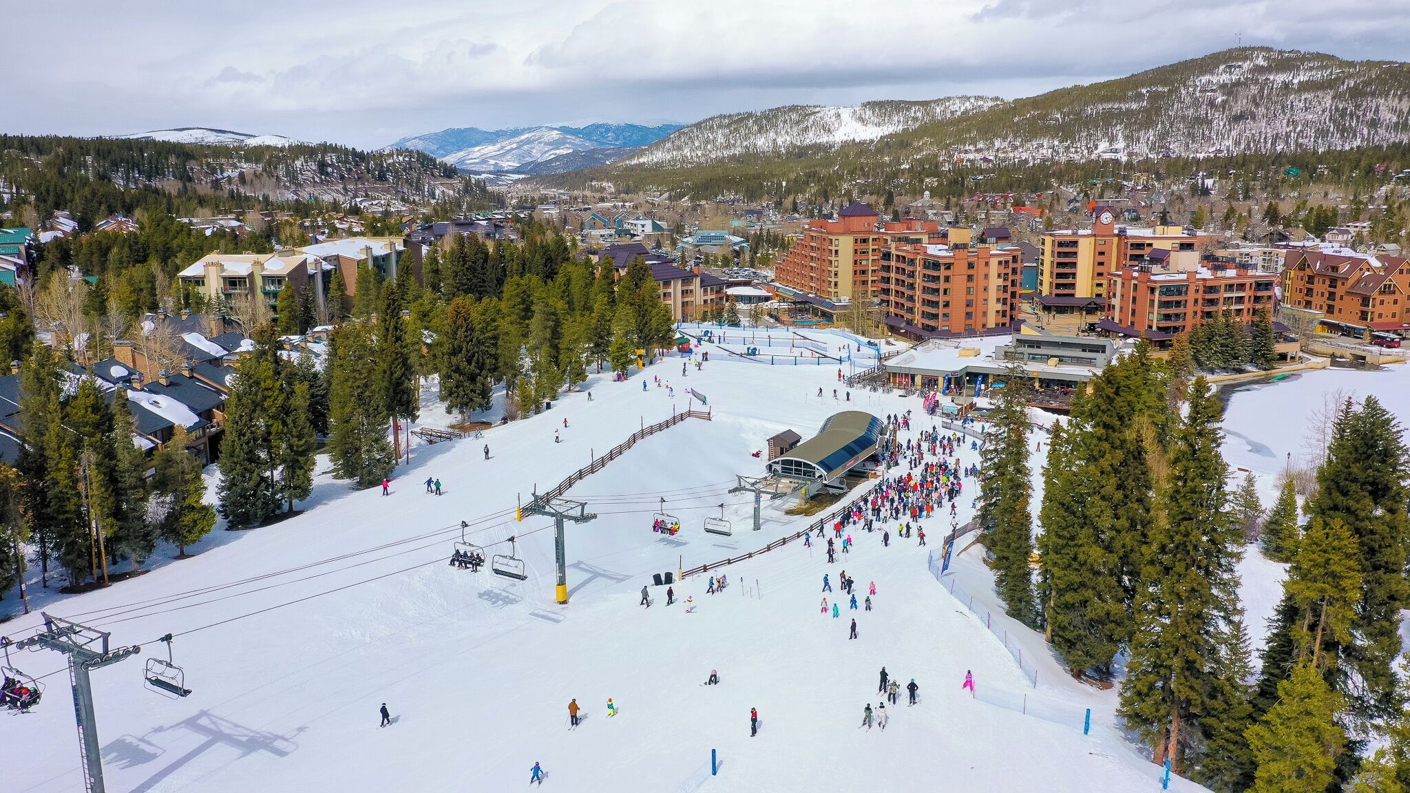 A ski resort with a ski lift, buildings, and a snowy mountain backdrop.