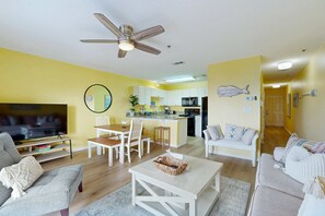A living room with a TV, sofa, coffee table, and a dining area with chairs and a table. - Coastal condo with free WiFi, on-site pool & hot tub (Santa Rosa Beach)