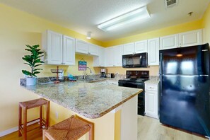 A kitchen with white cabinets, a granite countertop, a black refrigerator, and a microwave. - Coastal condo with free WiFi, on-site pool & hot tub (Santa Rosa Beach)
