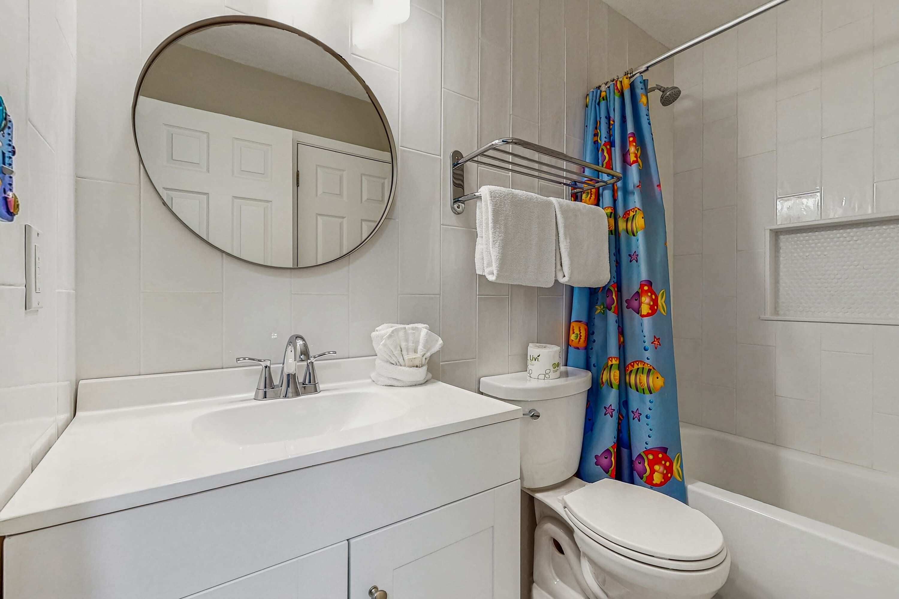 A bathroom with a white sink, mirror, and toilet. There is a shower curtain with a fish pattern.