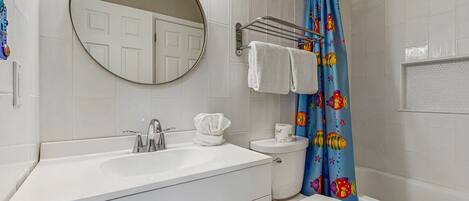 A bathroom with a white sink, mirror, and toilet. There is a shower curtain with a fish pattern.