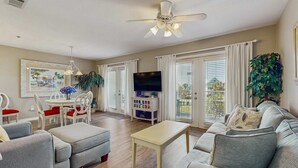 Uma sala de estar com sofá, mesa de centro, painel para TV e um espaço de jantar com cadeiras e mesa.
