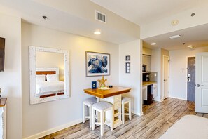 A room with a bed, a desk, two chairs, a painting, and a door leading to a bathroom. - Stunning ocean view studio in Luau I with resort pool & tram pass - near beach (Miramar Beach)