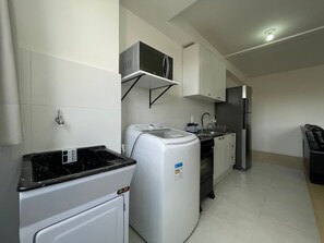 A compact kitchen with a washing machine, a microwave, and a refrigerator. - Solarium Beach Club - Apartamento T1.302 (Itapoá)