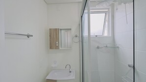 Een moderne badkamer met een douchecabine van glas, een houten wastafelmeubel en een klein raam.