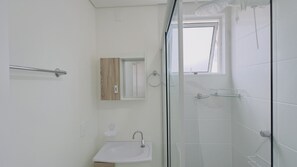 A modern bathroom with a glass shower enclosure, a wooden vanity, and a small window. - Solarium Beach Club - Apartamento T1.302 (Itapoá)