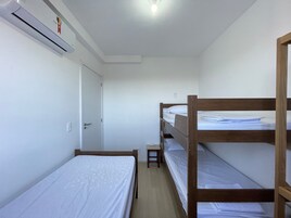 Um dormitório com beliches, uma porta, um aparelho de ar condicionado e um banquinho pequeno.