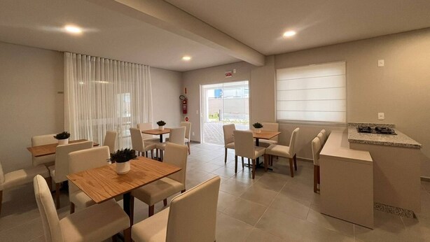 A modern dining area with multiple tables and chairs, a kitchen counter, and a fire extinguisher. - Solarium Beach Club - Apartamento T1.302 (Itapoá)