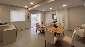 Une chambre d’hôtel moderne dotée d’un coin repas, d’un comptoir de réception et d’une fenêtre avec des rideaux.