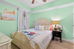 Un dormitorio con una cama, una mesita de noche, una lámpara y una pared con un cartel que dice 'Beach'.