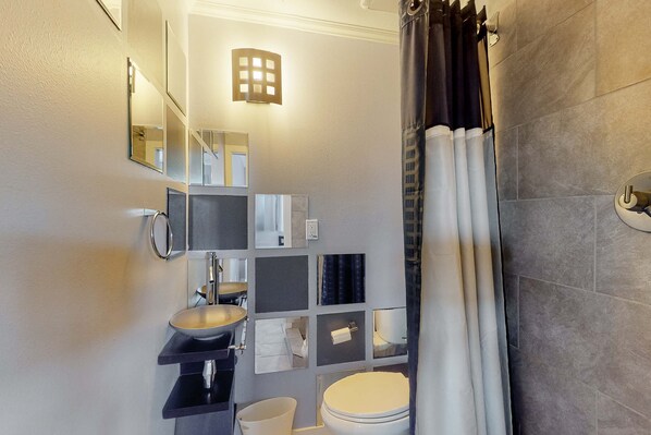 Un baño moderno con inodoro, lavamanos y espejo. Hay varios espejos y una lámpara en la pared.