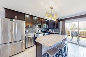Una cocina moderna con electrodomésticos de acero inoxidable, armarios oscuros, una isla de granito y una puerta corredera de vidrio a un patio.